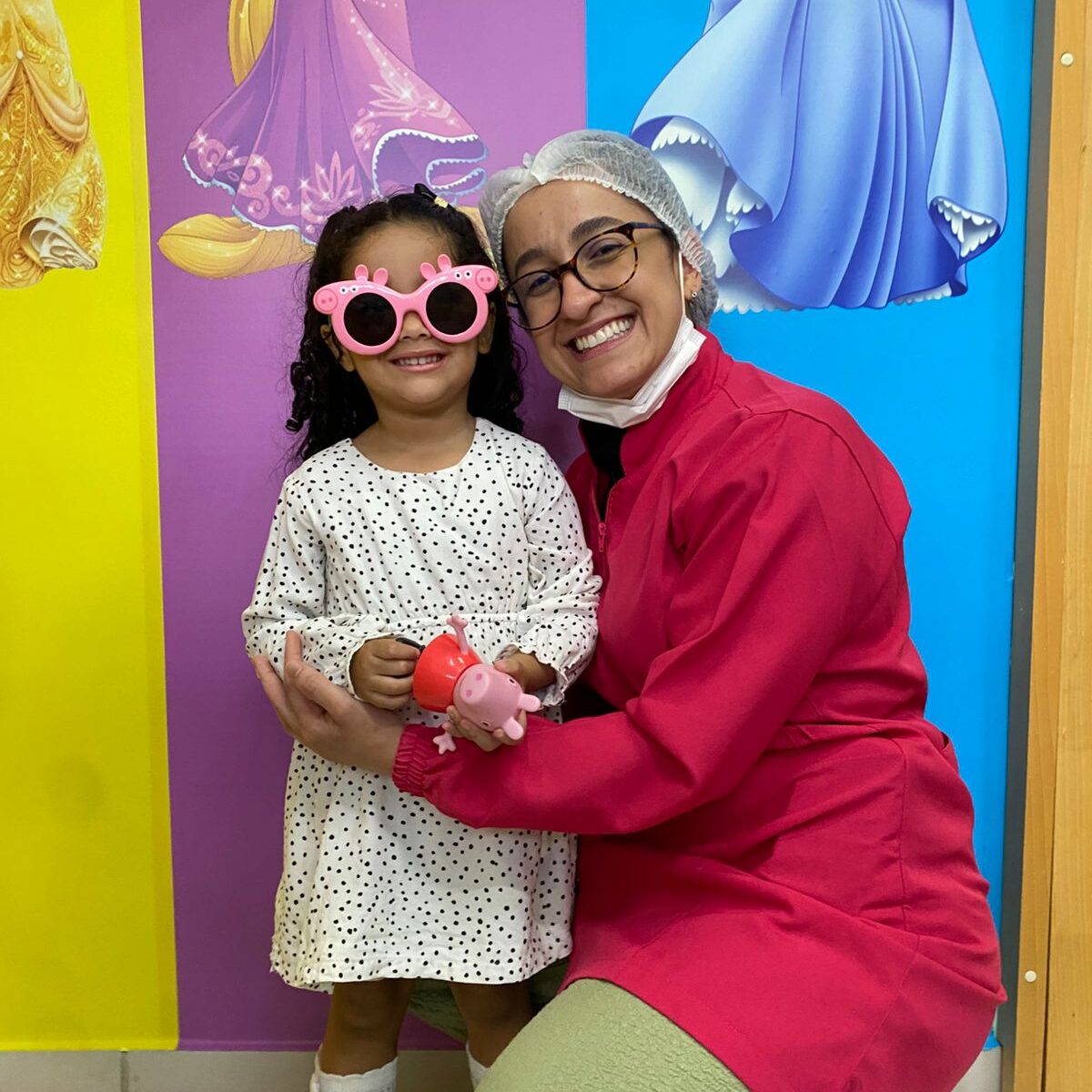 Ortodontista com paciente criança usando óculos divertidos em consultório de ortodontia infantil com ambiente lúdico