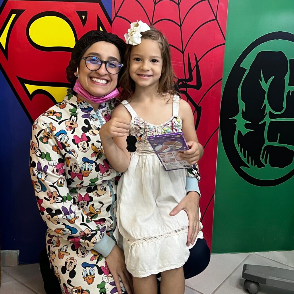 Ortodontista sorrindo ao lado de paciente infantil em consultório de ortodontia infantil decorado com super-heróis